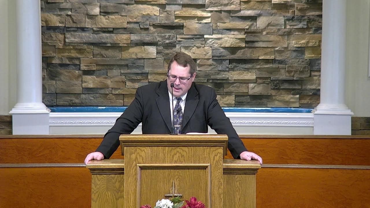 Pastor Paul Harvey preaching from the oak pulpit at Countryside Baptist Church, with the stacked-stone wall behind him.